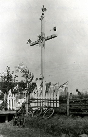 Croix de chemin ornemente d'un soleil  l'axe et d'un coq  la cime et agrmente de drapeaux papal. Saint-Franois, Qubec, 1923., © MCC/CMC, Edouard Zotique Massicotte, 60026