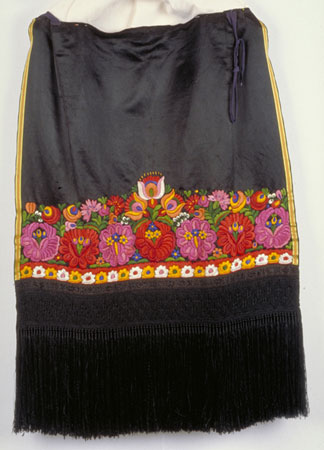 Tablier en satin et en coton au motif floral brodé multicolore. Sa partie inférieure est richement décorée de dentelle noire et d'une longue frange. Il a été confectionné en Hongrie vers 1920., © MCC/CMC, 76-515.5