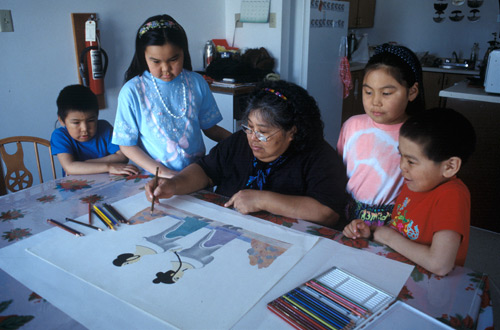 Pitaloosie Saila, entourée d'enfants, utilisant des crayons de couleur pour dessiner ce qui allait devenir une estampe représentant deux femmes Pitaloosie Saila, entourée d'enfants, utilisant des crayons de couleur pour dessiner ce qui allait devenir une estampe représentant deux femmes
