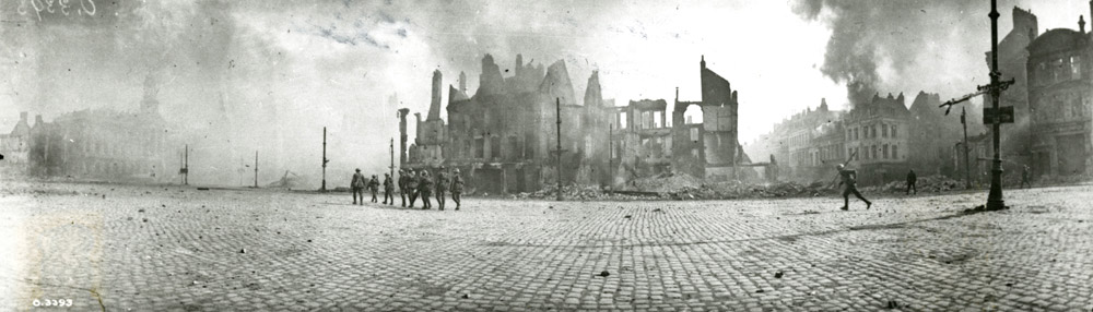 Photographie en noir et blanc de soldat passant devant les vestiges de bâtiments brulés