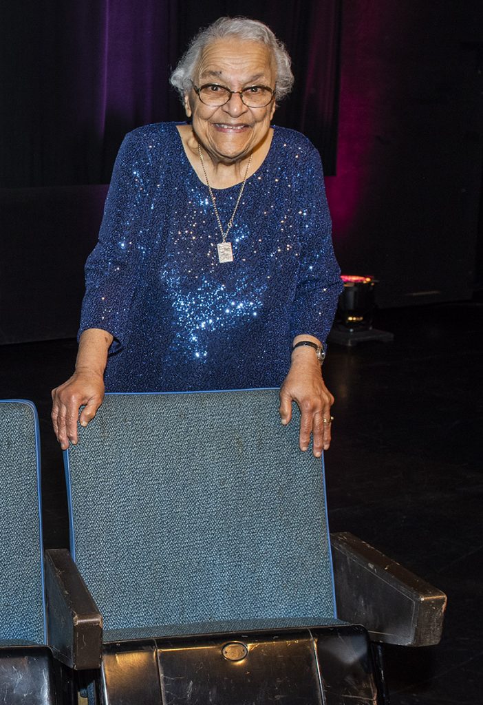 Une femme âgée souriante s’appuie sur un strapontin bleu rembourré