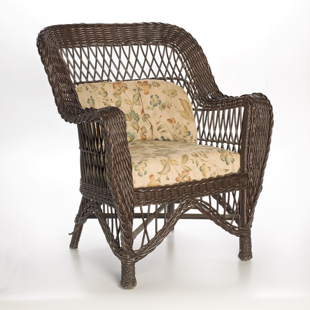 Un fauteuil en osier tressé et coussins de siège de couleur crème, ornés d’un motif floral