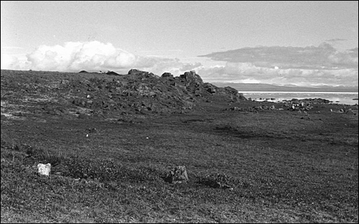 Vue panoramique d'un champ avec une formation rocheuse dans un coin et un cours d'eau dans l'arrière plan.