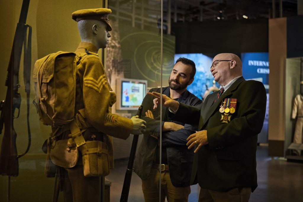 Visiteurs examinant un uniforme exposé dans la Gallerie du Musée canadien de la guerre