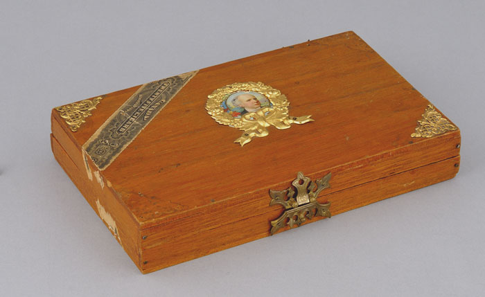 Ancienne boîte à cigares en bois ornée de dorures et d’un portrait en couleur de Laurier serti dans un cadre ovale de métal doré. Musée canadien de l’histoire, 2011.21.345