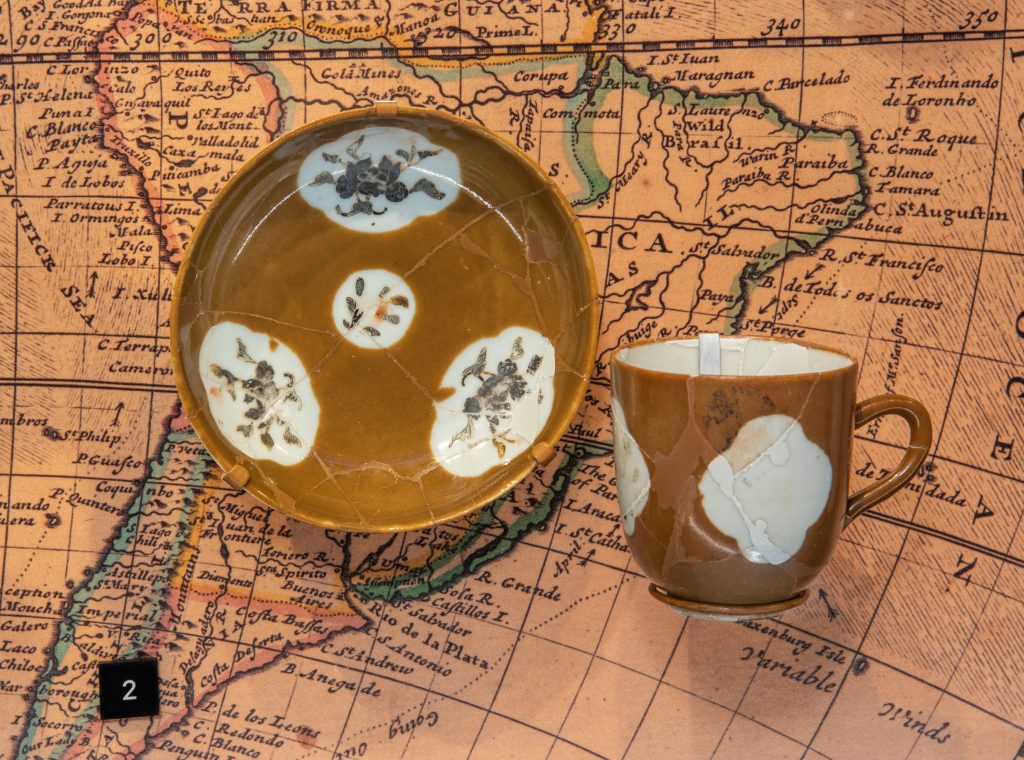 Tasse et soucoupe de porcelaine d’exportation chinoise de style « café au lait ». Les cartouches étaient à l’origine ornées de décors émaillés, qui se sont détériorés par les éléments. Retrouvées sur le site du Machault, qui a sombré en 1760. Prêt de Parcs Canada.