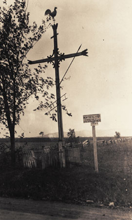 Croix de chemin ornemente d'un coq, d'une lance et d'une chelle sur la hampe. Sainte-Madeleine, Qubec, 1923., © MCC/CMC, Edouard Zotique Massicotte, 60067