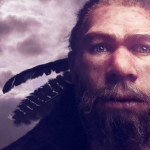 A bearded man in Ottawa, standing in front of the Canadian Museum of History, with feathers in front of a cloudy sky.