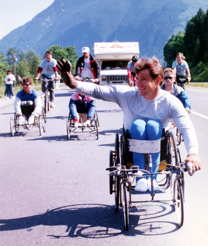 Des personnes en fauteuil roulant et à bicyclette sur une route pavée