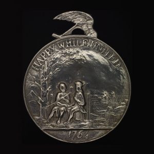 Médaille circulaire représentant deux personnages assis côte à côte, avec les mots « Happy while united » (« Heureux et unis ») et l’année 1764.