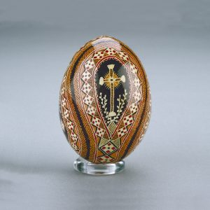 Un œuf de Pâques ukrainien décoré d’un délicat motif de diamants rouges, noirs, bruns et oranges disposés autour d’une croix centrale.