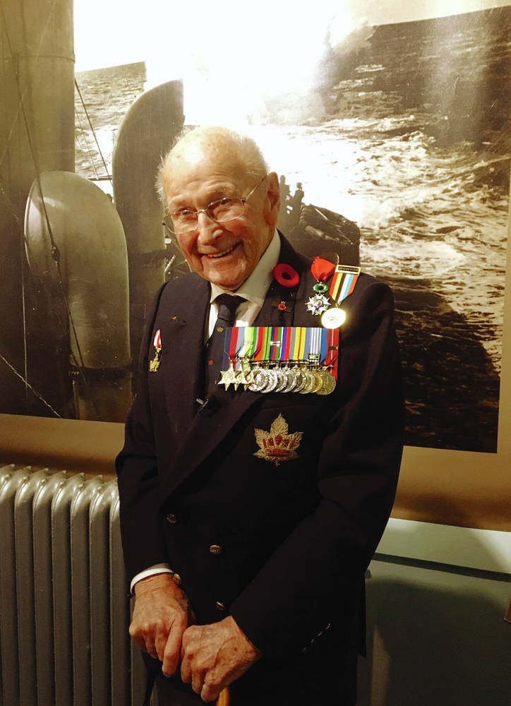 A decorated military veteran wearing a suit smiles while resting his hands on a cane.