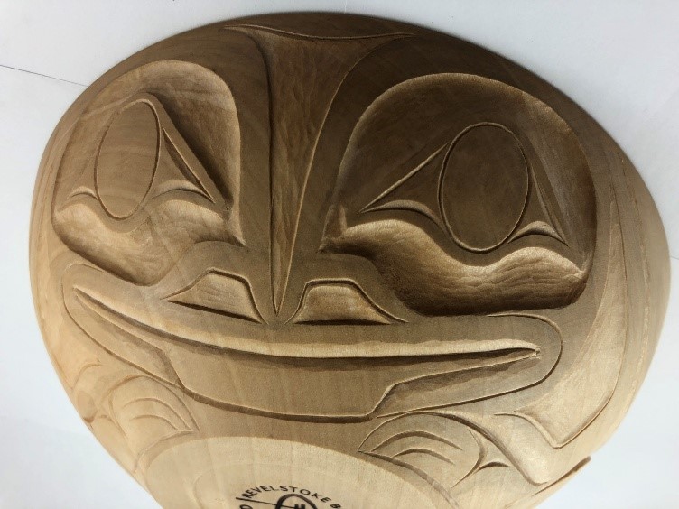 Un grand bol en bois sur la paroi extérieure duquel est sculptée une tête de grenouille stylisée.