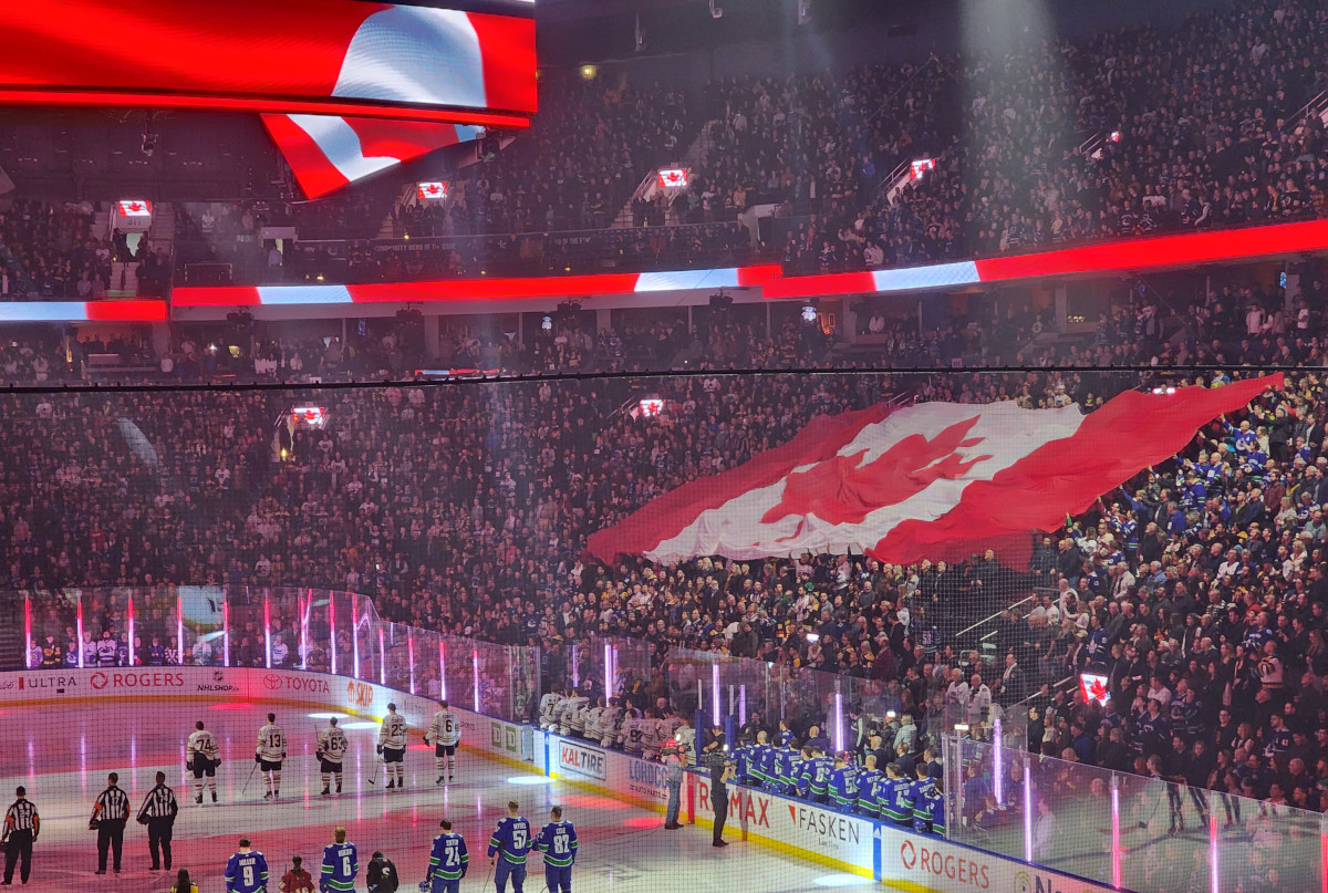Dans un stade bondé, un énorme drapeau flotte au-dessus de la foule tandis que tous les yeux sont braqués sur les joueurs de hockey et les arbitres alignés sur la glace.