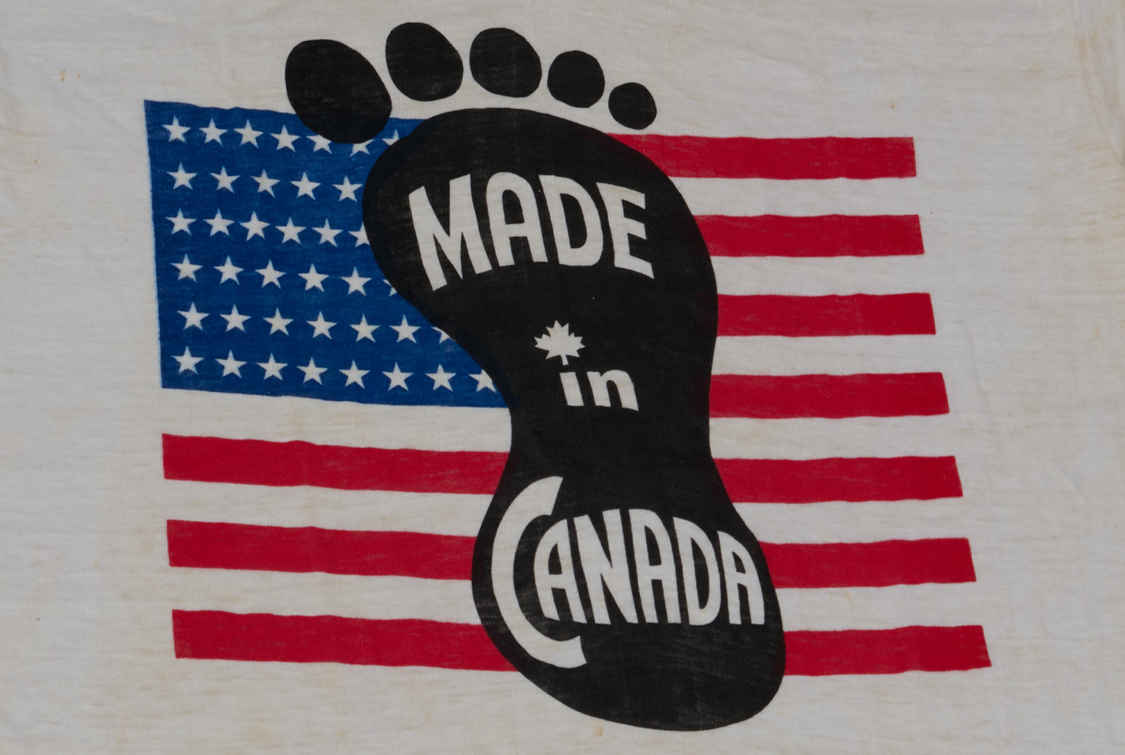 Une empreinte de pied noire et du texte blanc qui dit « Made in Canada » (Fait au Canada), écrasant un drapeau américain.
