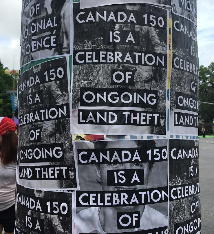 Un poteau téléphonique couvert de prospectus sur lesquels on peut lire « Canada 150 is a celebration of ongoing land theft. » (Canada 150 est une célébration du vol de terres qui se poursuit encore.)