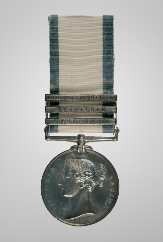 Une médaille de couleur argentée, suspendue à un ruban orné de trois barrettes métalliques gravées.
